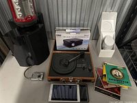 Overall view of the audio turntable, boxed Naxa speaker, vinyl records, and some electronic devices including a tablet and small camera.