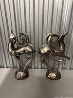 Front view of two silver-colored modern abstract deer figurines with detailed spiral antlers and geometric bases.