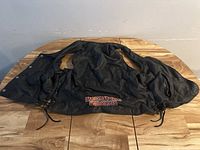 Full view of black leather vest spread flat showing front and sides with lace-up sides and snap buttons