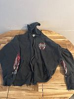 Full view of black zip-up Harley Davidson hoodie sweater laid flat showing flame designs on sleeves and chest logo.