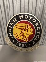 Photo showing the round metal sign with Indian Motorcycle logo, year 1901, and 'Premium Cigar' banner below