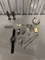 Full view of all jewelry and watches on display including goblets, coins, flask, lighter, and chain necklace.