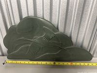 Dark green marble artwork hand-carved with two flying birds in relief, placed against a metal backdrop with measuring tape showing approx 20 inches width.