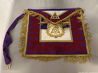 Full view of the Masonic satchel showing the purple and red fabric, gold embroidered symbols, gold fringe edges, and purple shoulder strap with gold clasp.