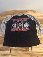 Black and grey raglan long sleeve shirt with Ratt band graphic and text 'Today the Cellar... Tomorrow the World' shown front view on wooden table.