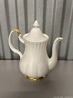 Front and side view of white bone china teapot with gold accents on handle, spout, base and lid finial.