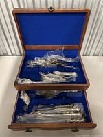 Silverware set inside an open wooden chest with blue velvet lining, utensils mostly wrapped in plastic.