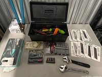 All items laid out on table including toolbox, various tool sets in packaging, adjustable wrenches, and screwdriver bits.