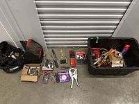 Overall lot laid out including tool bags, plastic bin, hand tools, and hardware items organized on floor in front of storage unit door.