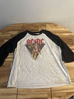 Full view of AC/DC raglan t-shirt laid flat on table showing black sleeves and white body with graphic on front.