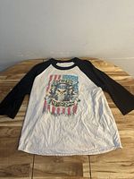 Full front view of the long sleeve shirt laid flat on wooden surface, showing graphic of skull with guns and the American flag.