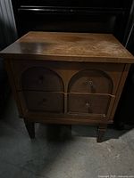 Front view of vintage wooden nightstand with four drawers, showing wear on the wood surface and drawer fronts