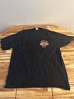 Full front view of the black XL Harley Davidson T-shirt laid flat on wooden surface, showing overall condition