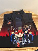 Full view of front of black button-up shirt showing large graphic of a male and female biker on motorcycles with a red sunset background.