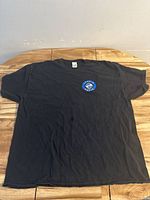 Front view of black t-shirt on wooden surface, showing the overall shirt condition and shape.
