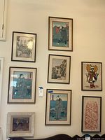 Wall display of eight art pieces including three Asian woodblock prints, two black and white cityscape sketches also framed, and two fabric art pieces plus one small painting.