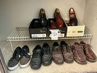 Overall view of all eight men's shoes arranged on closet shelf, showing dress shoes in original boxes and several pairs of casual and athletic shoes in front.