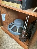 Speaker driver on wooden shelf with visible label and power cable wrapped