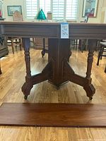 Side view of the table pedestal and one leg showing turned wood carvings and caster wheels, with removable leaf placed in front.