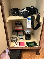 Group of cameras and Pentax lens boxes on two-tier shelf