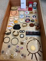 Overview of costume jewelry collection laid in a wooden drawer including buttons, pins, bracelets, earrings, rings, a coin purse, and the wooden bead necklace