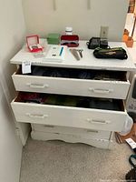 Side view of vintage white wooden dresser with four drawers, showing paint chips and wear, some drawers partially open with textiles inside.
