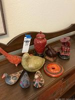 Wide shot showing full lot with all bird figurines, metal vase, and wooden statue on wooden surface against wall.