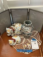 Set of all items including three gold-decorated ceramic cats, multicolored ceramic vase, and tri-fold picture frame on crocheted doily.