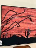 Framed fabric art showing red sky and black cactus silhouettes