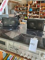 Two black Omega speakers placed on a table with a Hitachi stereo cassette recorder underneath, showing overall lot items.