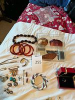 Photo showing assortment of jewelry laid on white cloth: brown bangles, brown necklace, silver and turquoise brooches, earrings, colorful braided bracelet, hair combs and pins