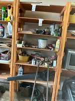 Wooden shelving unit with assorted miscellaneous garage items including gardening tools, blower, and hardware items arranged on shelves.