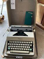 Olympia Deluxe typewriter in beige color inside its hard carrying case and green instruction booklet inside case lid