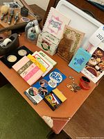 Table display of vintage recipe books, Blu-Tack, boxes, jewelry pieces, and cutters