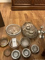 Overall lot showing candlestick holders, glass ashtrays, silver serving dish, creamer, and sugar bowl on wooden floor