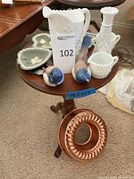 Full view of small wooden table with assorted items on top including Wedgwood trays, white glassware, bird figurines, and Jell-O mold on base