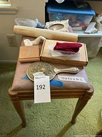 Photo showing small wooden bench with padded pink upholstery, various vintage items including ornate silver hand mirror, red mittens, tobacco pipe, albums, and documents placed on top.
