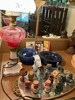 26 inch vintage glass lamp with pink base and white frosted glass shade. Blue glass dishes and vintage party pamphlets in the background. Mirrored tray with figurines in foreground.