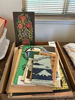 Top view of a pile of vintage sheet music and song folios on a table including a distinct green 'Nick Manoloff Spanish Guitar Method' cover and a blue 'Joyful Singing Campfire Girls Edition' songbook.
