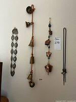 Full view of all items: metallic wall bells strand, copper and blue bead hanging ornament, metal clasp belt, and bolo tie with boot charm, all hanging on wall.
