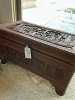 Angle showing top and side carved relief scenes of the wooden chest with detailed Asian motifs