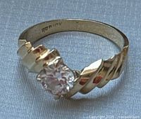 Full view of gold ring with twisted band and round clear CZ stone set in prongs.