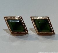 Close-up of the square-shaped earrings showing green stones and gold openwork border detail.