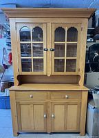 Full front view of two-piece pine cupboard showing upper glass doors and lower storage
