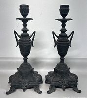 Front view of two intricately detailed antique Victorian spelter candlesticks with classical urn shapes and decorative bases.