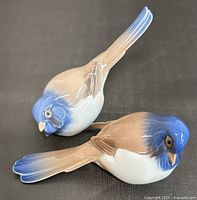 Two porcelain birds, one with vibrant blue head and brown wings, the other lighter blue and white, showing condition and detail.