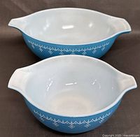 Two Pyrex mixing bowls arranged stacked showing blue exterior with white decorative pattern and white interior