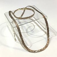Two-tone braided necklace and bracelet displayed on a clear stand showing length and design.