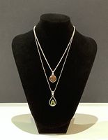 Two silver necklaces displayed on a black bust showing amber and green gemstone pendants.