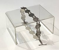 Silver bracelet laid on an acrylic display stand showing side view of medallion links and toggle clasp.